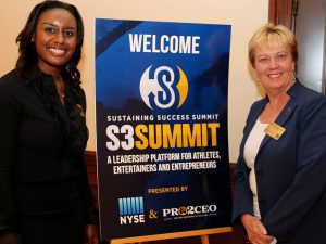 Two women standing next to a sign that says " sustaining success summit s 3 summit ".